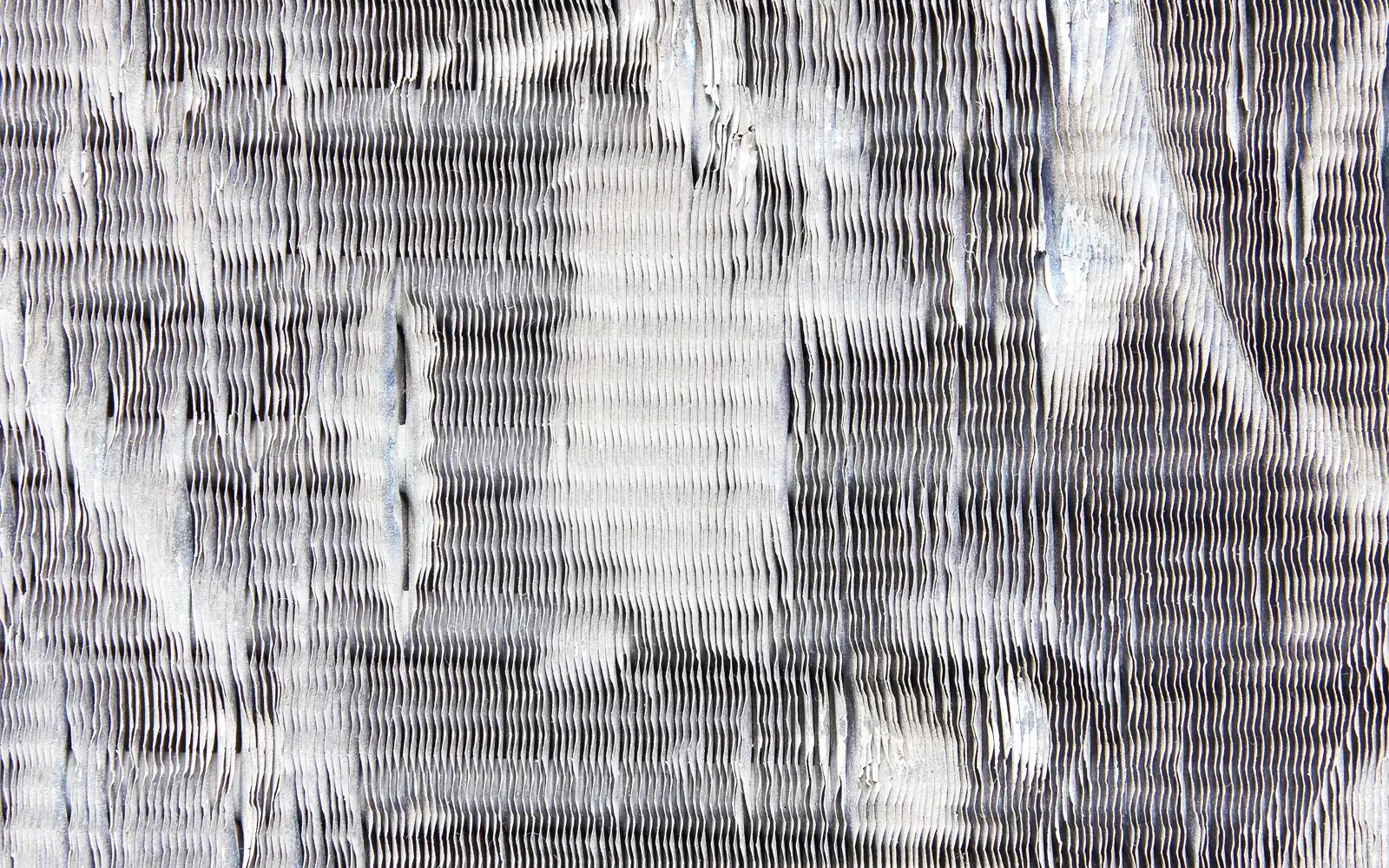 Close-up of an air conditioner condenser coil with its aluminum fins crushed and flattened by hail