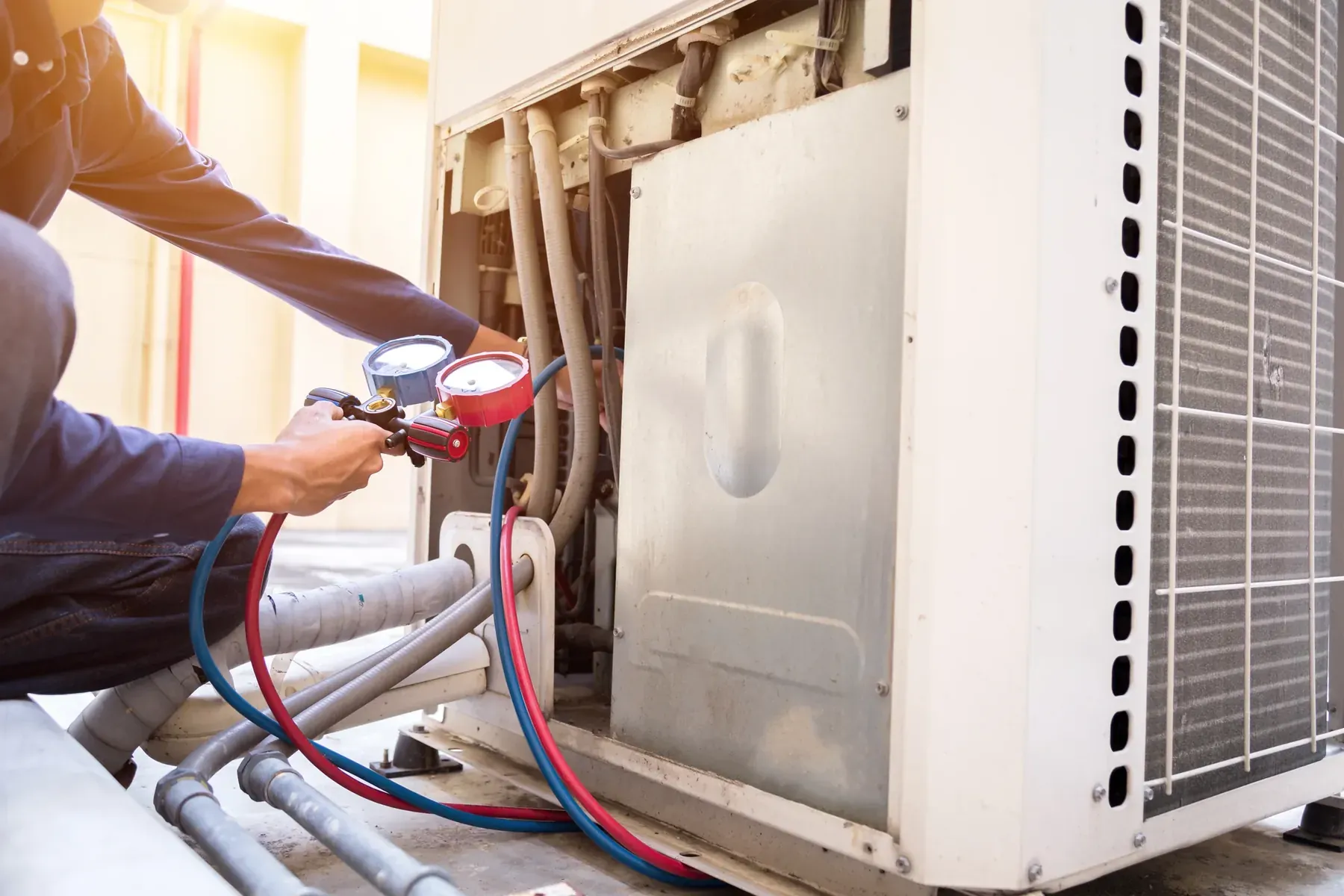 HVAC technician connecting a refrigerant gauge manifold to the service ports of an outdoor AC unit
